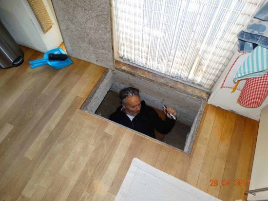 Inspecteur staat in een kelderluik onder een houten vloer