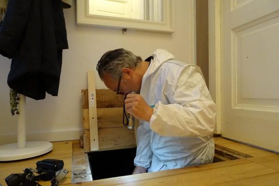 Inspecteur in witte overall bij een geopend vloerluik met een endoscoop