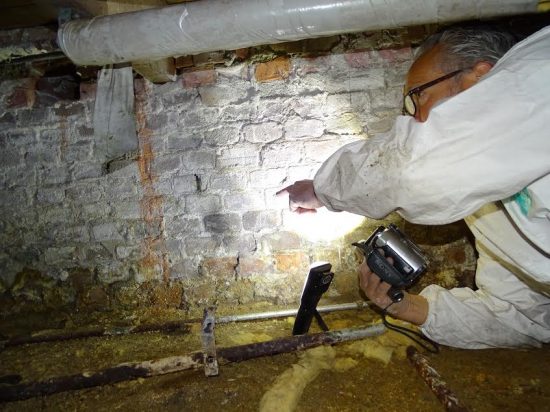 Inspecteur met een lamp bij een bakstenen kelderwand