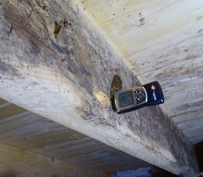 Vochtmeter op een houten vloerbalk met vochtplekken