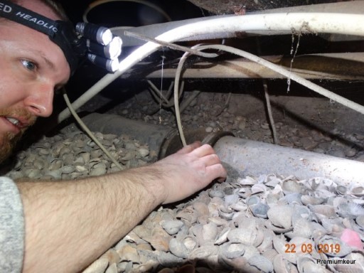 Hand op de schelpenlaag in een kruipruimte met leidingen