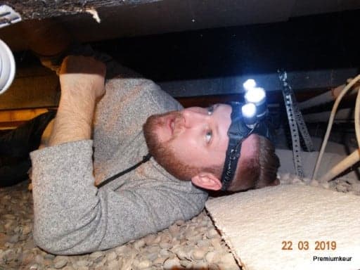 Inspector with a head torch lying in a crawl space